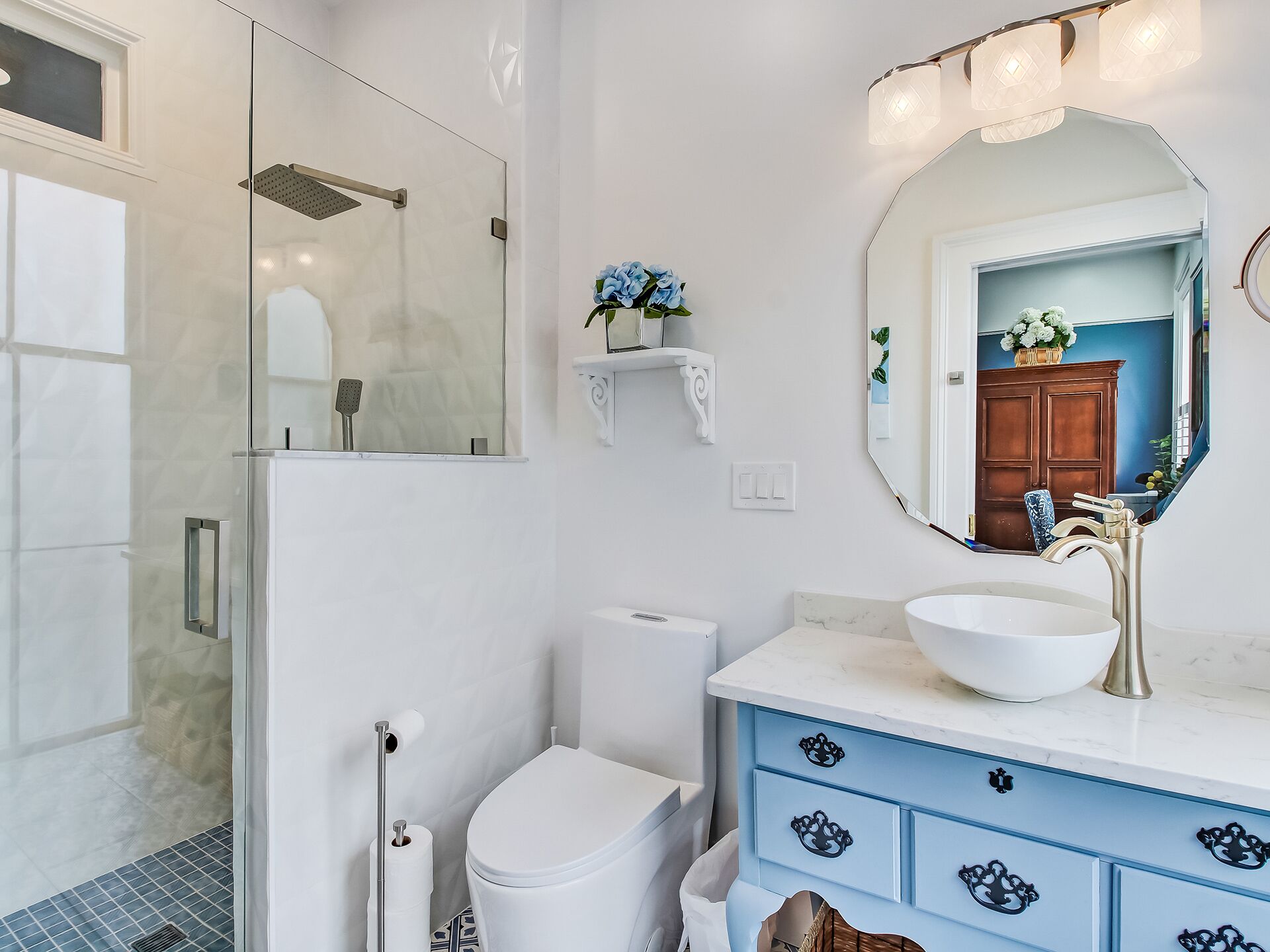Une salle de bain avec une douche à parois de verre, des toilettes blanches, un lavabo avec un receveur blanc et un meuble-lavabo avec des tiroirs bleus.