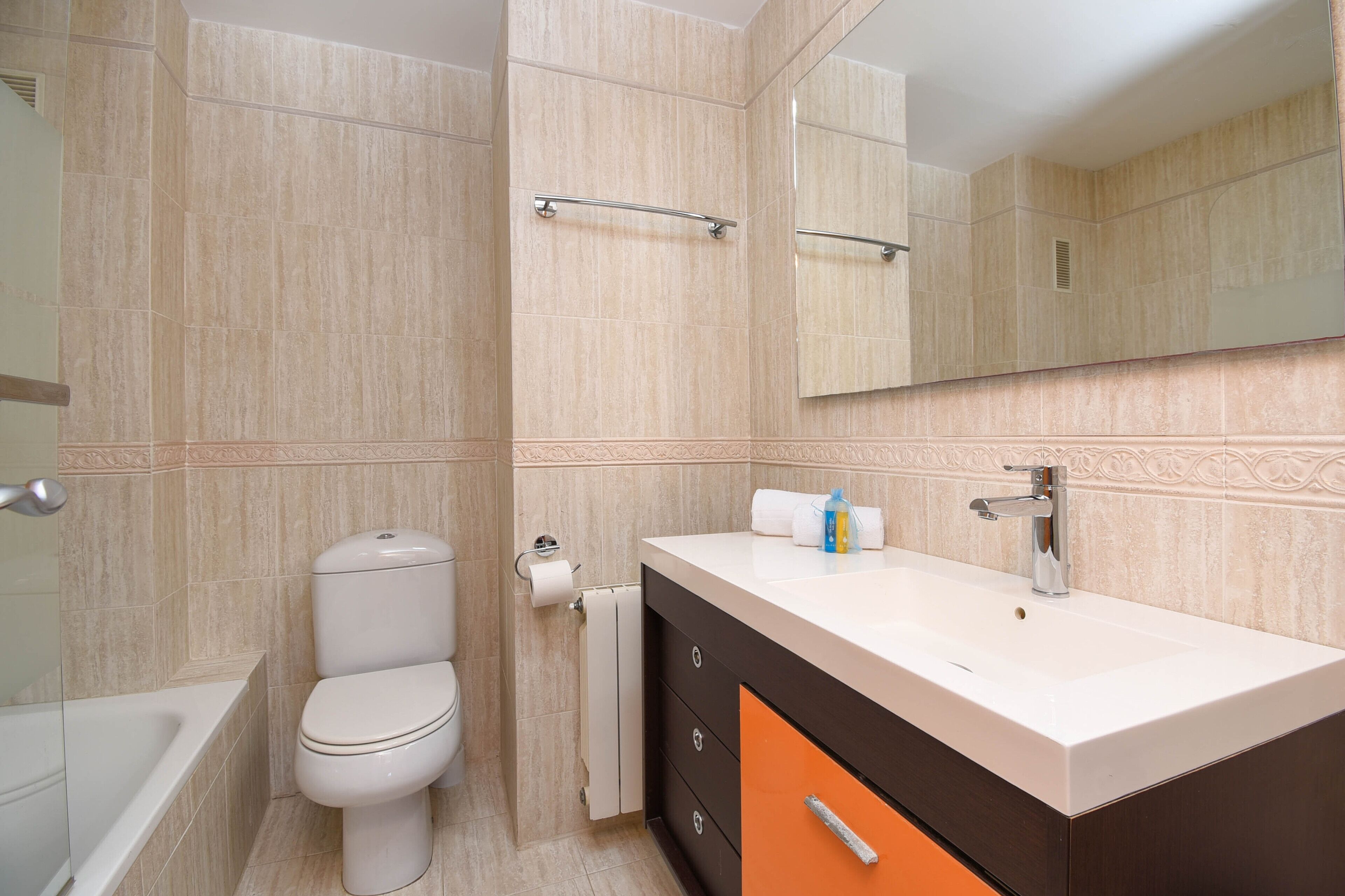 Een moderne badkamer met een wit toilet, een wastafel met spiegel, en een bad.