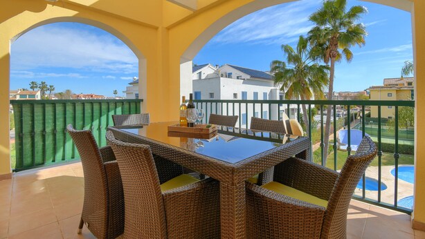 A balcony with wicker furniture and a glass table, overlooking a pool and palm trees. - Sorolla Sol - Javea, Costa Blanca (Javea)