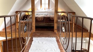 Un dormitorio en ático, con escalera de madera, cama con ropa de cama estampada y ventana que deja entrar luz natural.