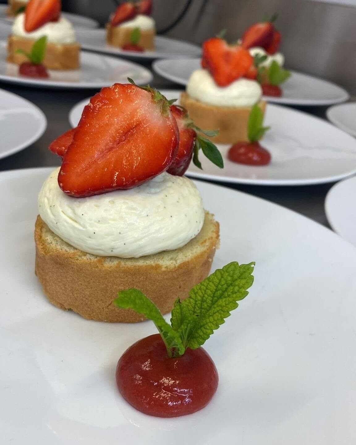 Un plato de postre con un pastelito cubierto de fresa y una hoja de menta como adorno.