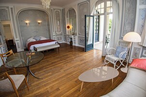 Une pièce spacieuse avec un grand lit, une table en verre, un fauteuil en osier et un canapé.