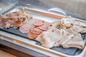 A display of various meats including sliced salami and prosciutto in a glass case. - Les Sorbiers (Hastiere)