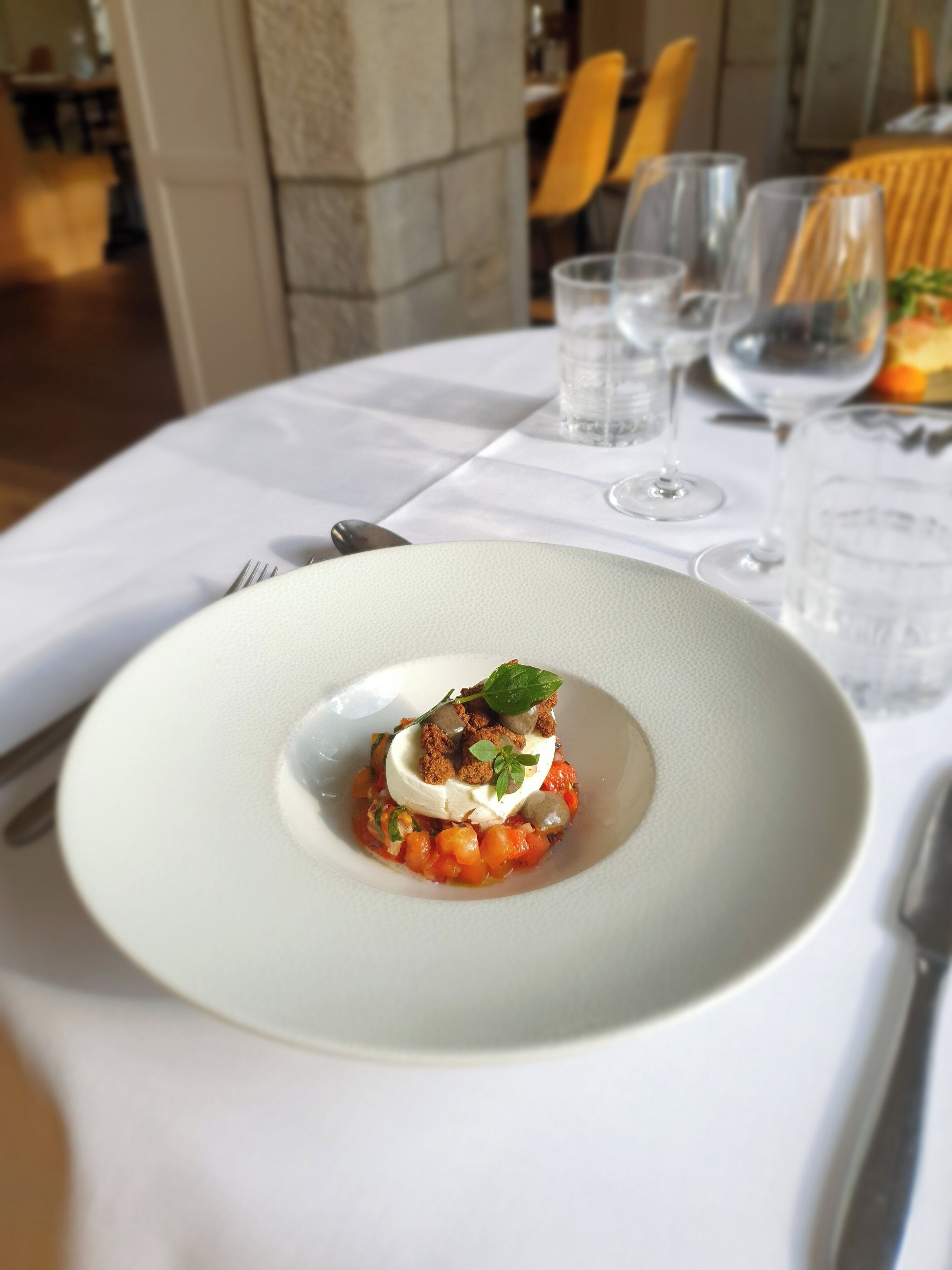 A dining table with a white tablecloth, a white plate with a dessert, and a glass of water.