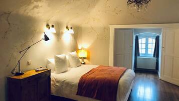 Une chambre à coucher avec un lit, des lampes de chevet, une table de nuit en bois, un lustre et une vue sur un couloir.