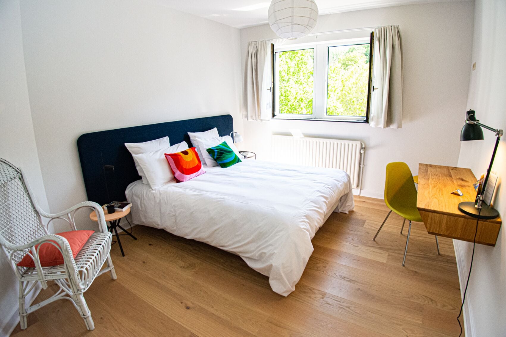 A bedroom with a bed, a desk, a chair, and a window with curtains.