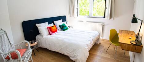 A bedroom with a bed, a desk, a chair, and a window with curtains.