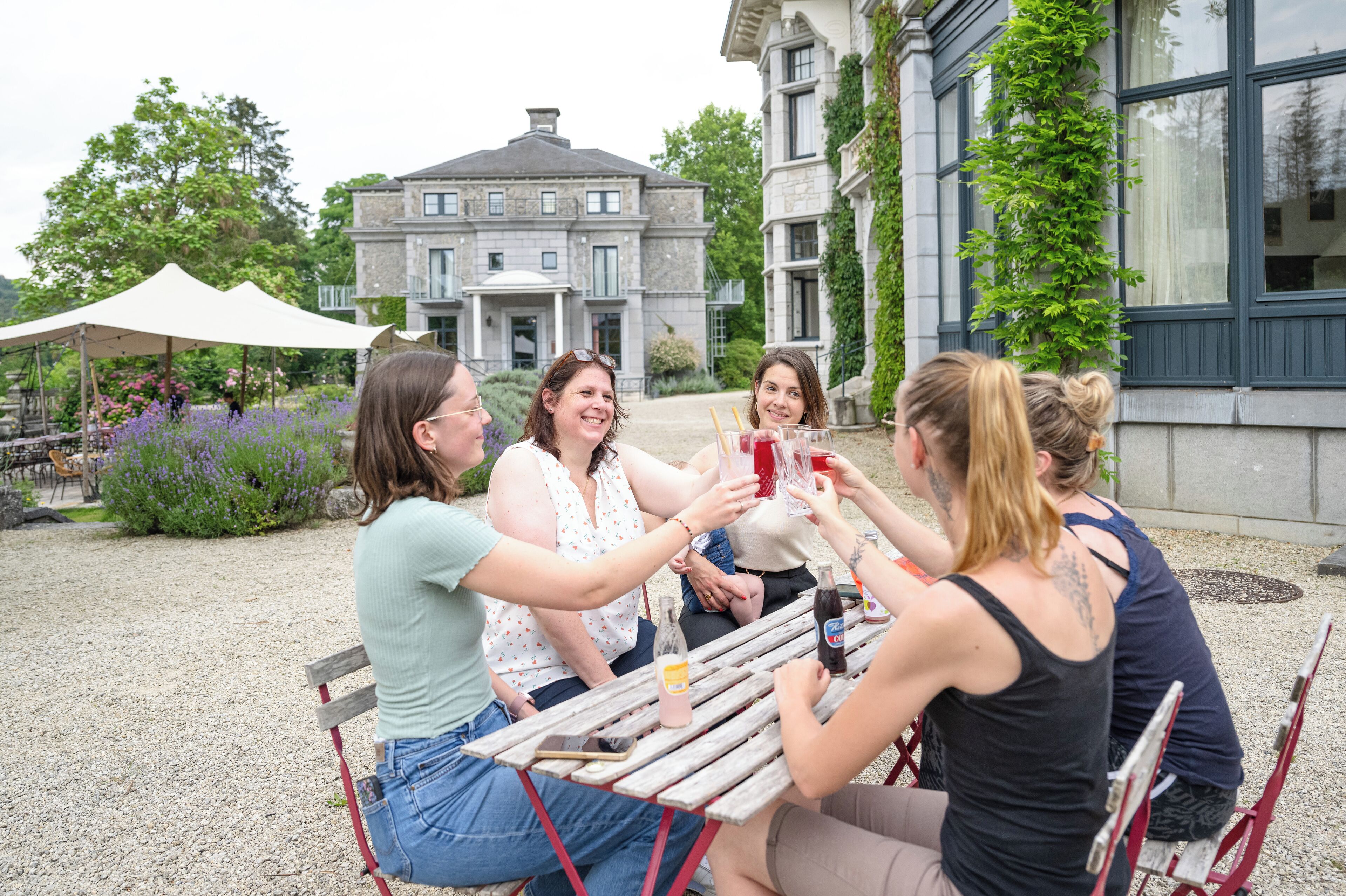 Un groupe de personnes porte un toast autour d’une table en bois, à l’extérieur, avec un bâtiment en arrière-plan.