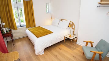 Een slaapkamer met een bed, nachtkastje, lamp, stoel en een raam met gordijnen.