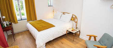 A bedroom with a bed, bedside table, lamp, chair, and a window with curtains.