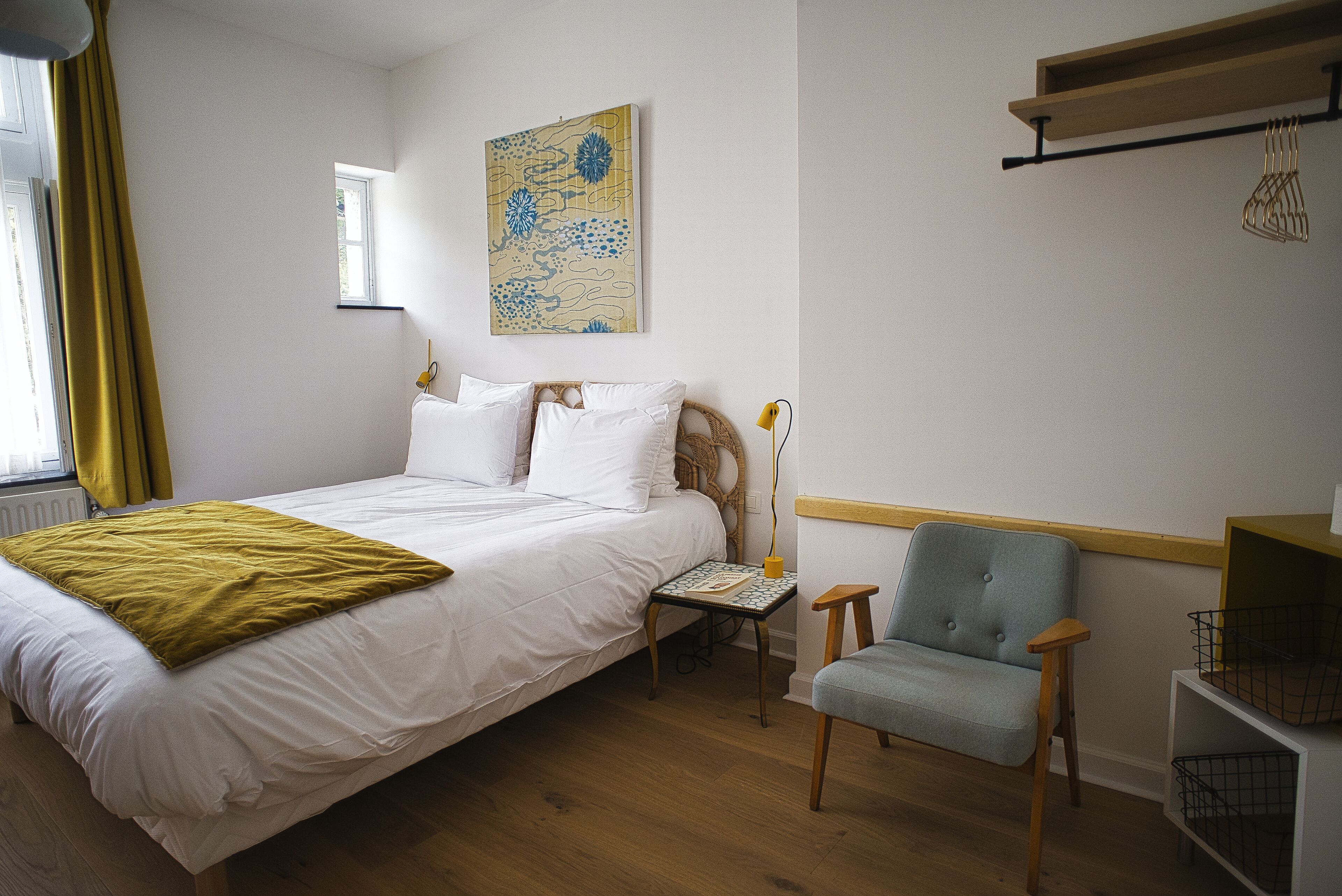 A bedroom with a bed, a chair, a small table, a lamp, and a wall art piece.