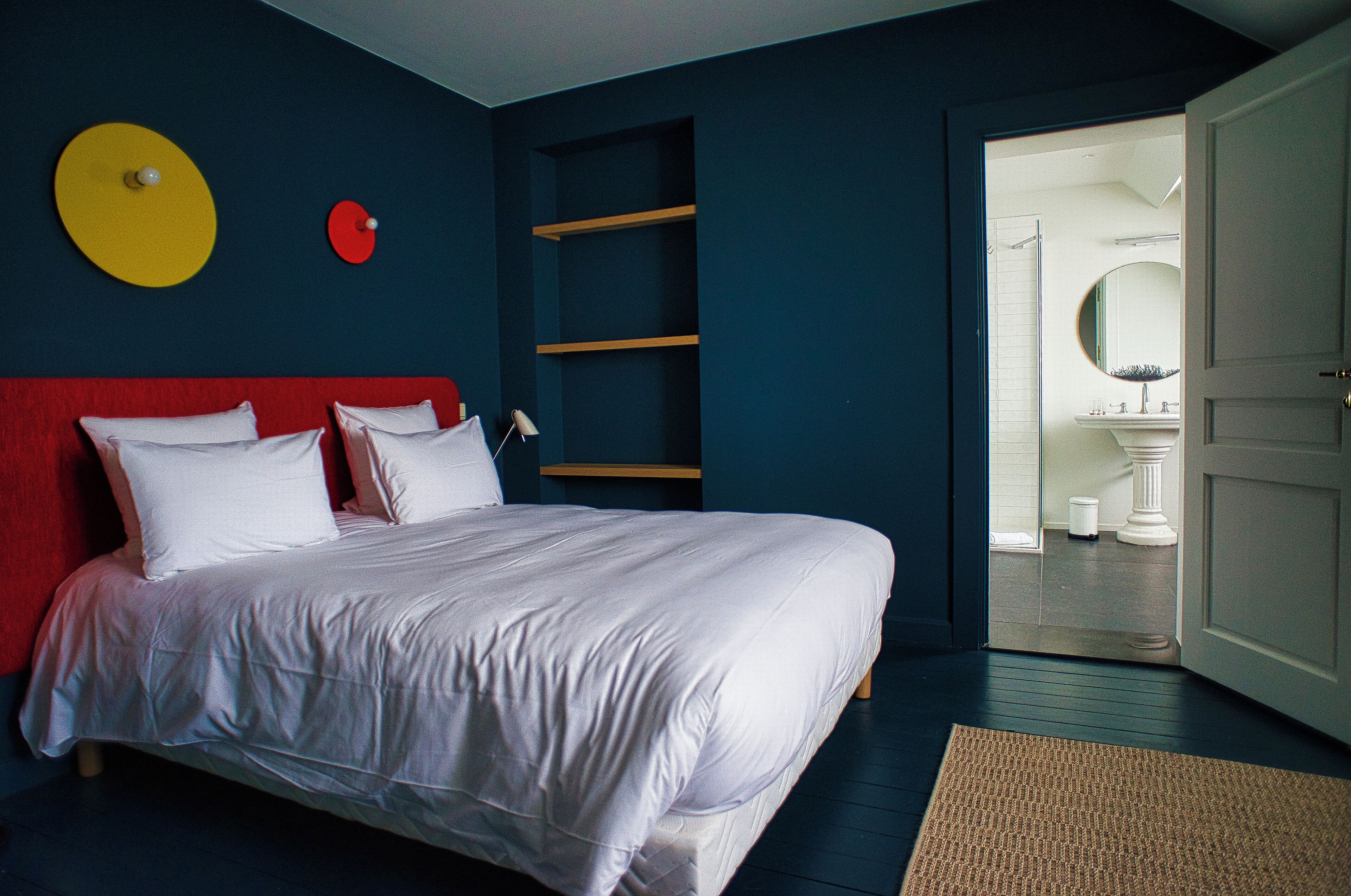 Une chambre à coucher avec un lit, une tête de lit rouge et un mur blanc orné d’un motif circulaire.