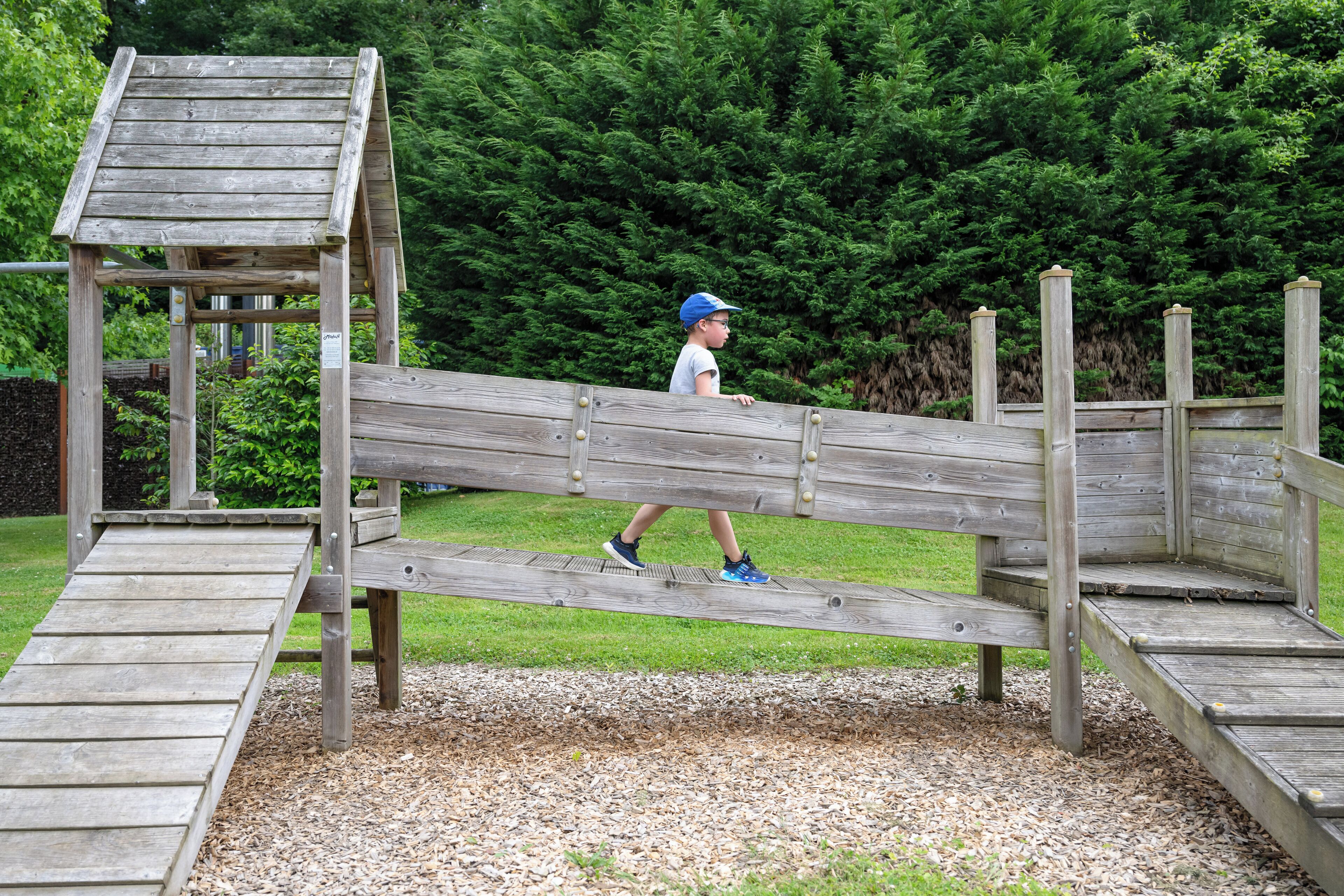 A wooden bridge in a park with a child walking across it.