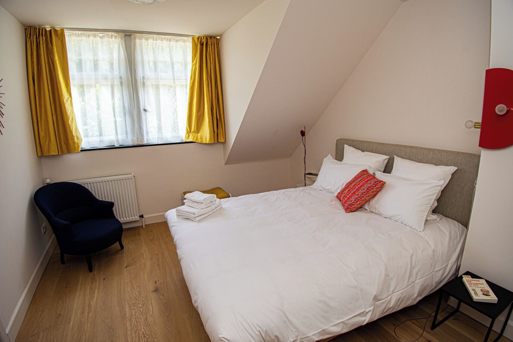 Une chambre avec un grand lit, une chaise, un radiateur et une fenêtre avec des rideaux.