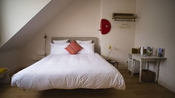 Un dormitorio con una cama grande, una mesita de noche, una lámpara colgante y un pequeño escritorio con una cesta.