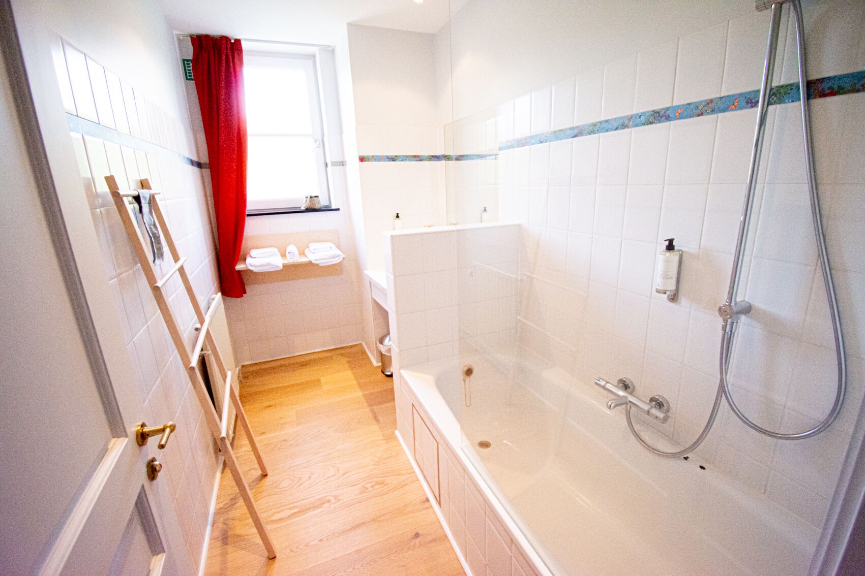 Une salle de bain avec une baignoire, une douche et une fenêtre ornée d’un rideau rouge.