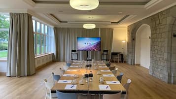 Un salón de conferencias con una larga mesa, sillas, un televisor y una pared de piedra.