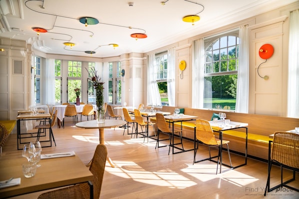 A spacious dining area with multiple tables and chairs, large windows, and a modern ceiling design. - Les Sorbiers (Hastiere)