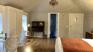 A bedroom with a bed, a desk with a chair, a piano, and a chandelier.