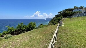 A coastal view with a grassy hillside, a wooden fence, and a building with a stone staircase.
