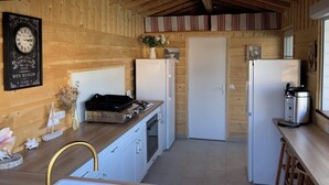 Une cuisine de taille réduite avec des murs en bois, une horloge ancienne, une cuisinière à gaz, un réfrigérateur et une machine à café.