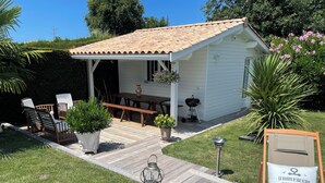 Une petite maison blanche avec un toit en tuiles, une terrasse en bois et du mobilier d’extérieur.