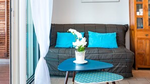 Une pièce avec un canapé sombre, une petite table ronde dont le plateau est bleu, et un vase blanc orné de fleurs.