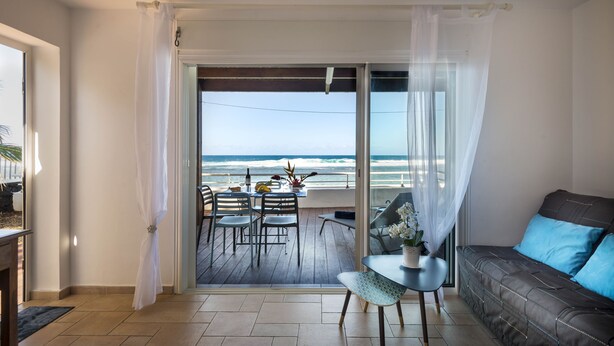Un balcon avec vue sur l’océan, une table à manger avec des chaises et un canapé avec des coussins.