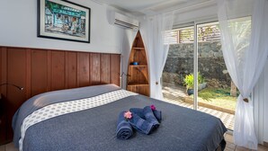 Une chambre avec un lit, un tableau encadré au mur, un appareil de climatisation et une vue sur l’extérieur par une porte vitrée.