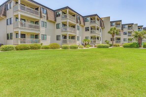 Un edificio residencial de varios pisos con balcones, un césped bien cuidado y palmeras.