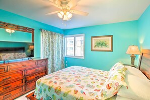 Un dormitorio con cama, cómoda, ventilador de techo, ventana con cortinas e imagen enmarcada en la pared.