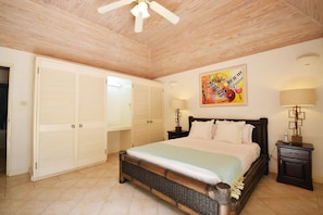 Une chambre à coucher avec un lit, un ventilateur de plafond, une armoire, un tableau et une table de chevet.
