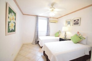 Une chambre d’hôtel avec deux lits, un ventilateur de plafond, une fenêtre avec des rideaux et un climatiseur fixé au mur.