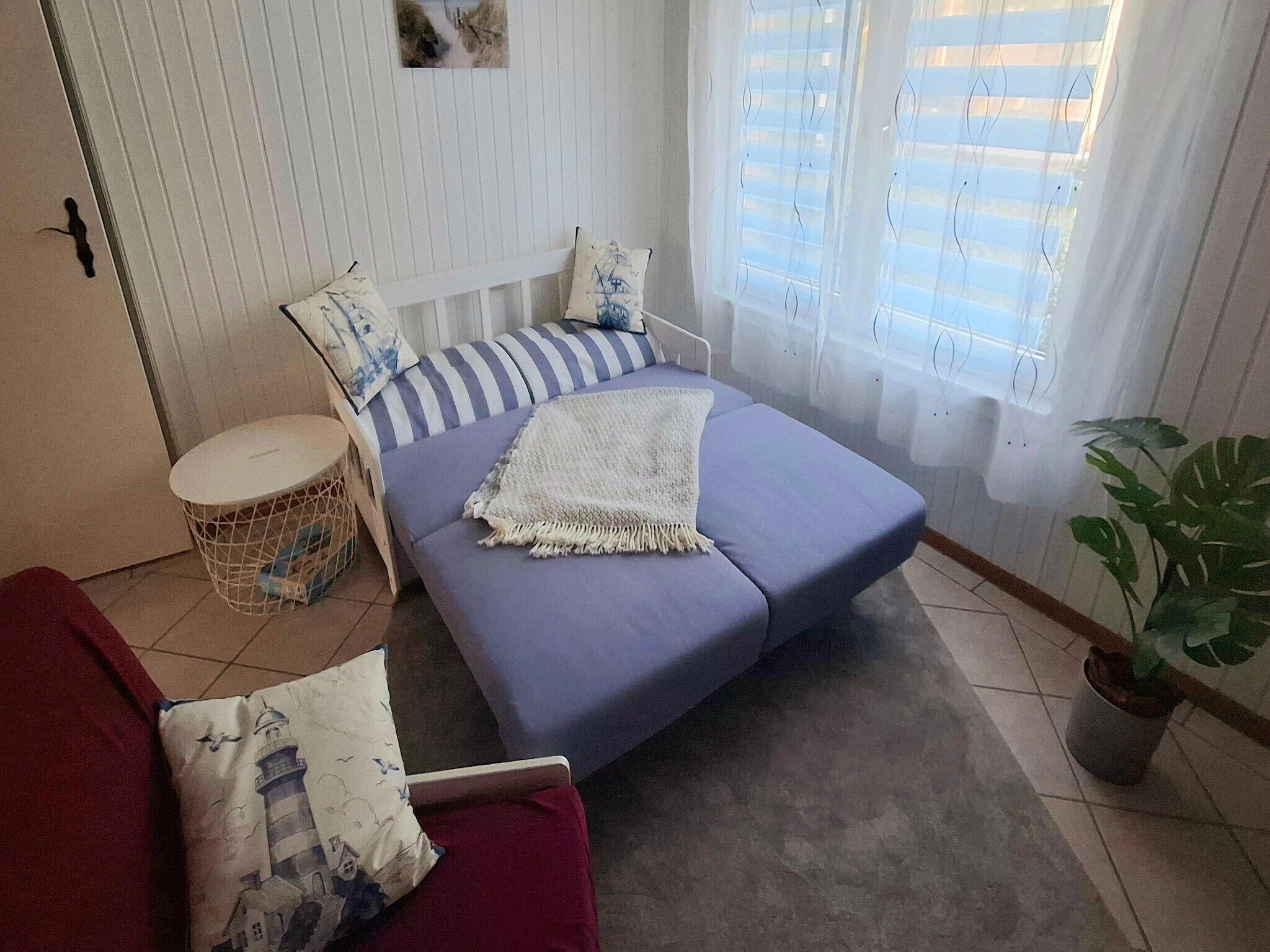 A small, cozy room with a bed, a red chair, a small round table, and a potted plant.