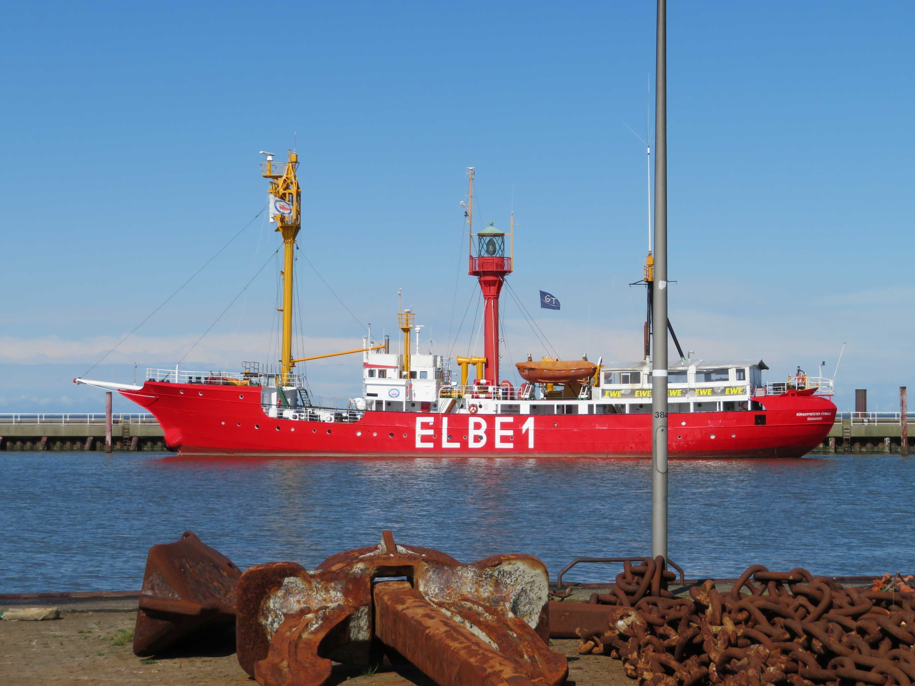 Ein großes rotes Frachtschiff liegt an einem Kai, auf dem man verrostetes Metallschrott sehen kann.