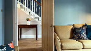 A living room with a beige sofa, a wooden door, and a staircase with white railings. - Luxury cottage in the heart of Craigellachie (Craigellachie)