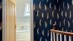 A room with a dark blue wall featuring a feather pattern, a wooden door, and a white bathtub. - Luxury cottage in the heart of Craigellachie (Craigellachie)
