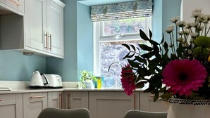 A modern kitchen with light grey cabinets, a wooden table, and a window with a view of greenery. - Luxury cottage in the heart of Craigellachie (Craigellachie)