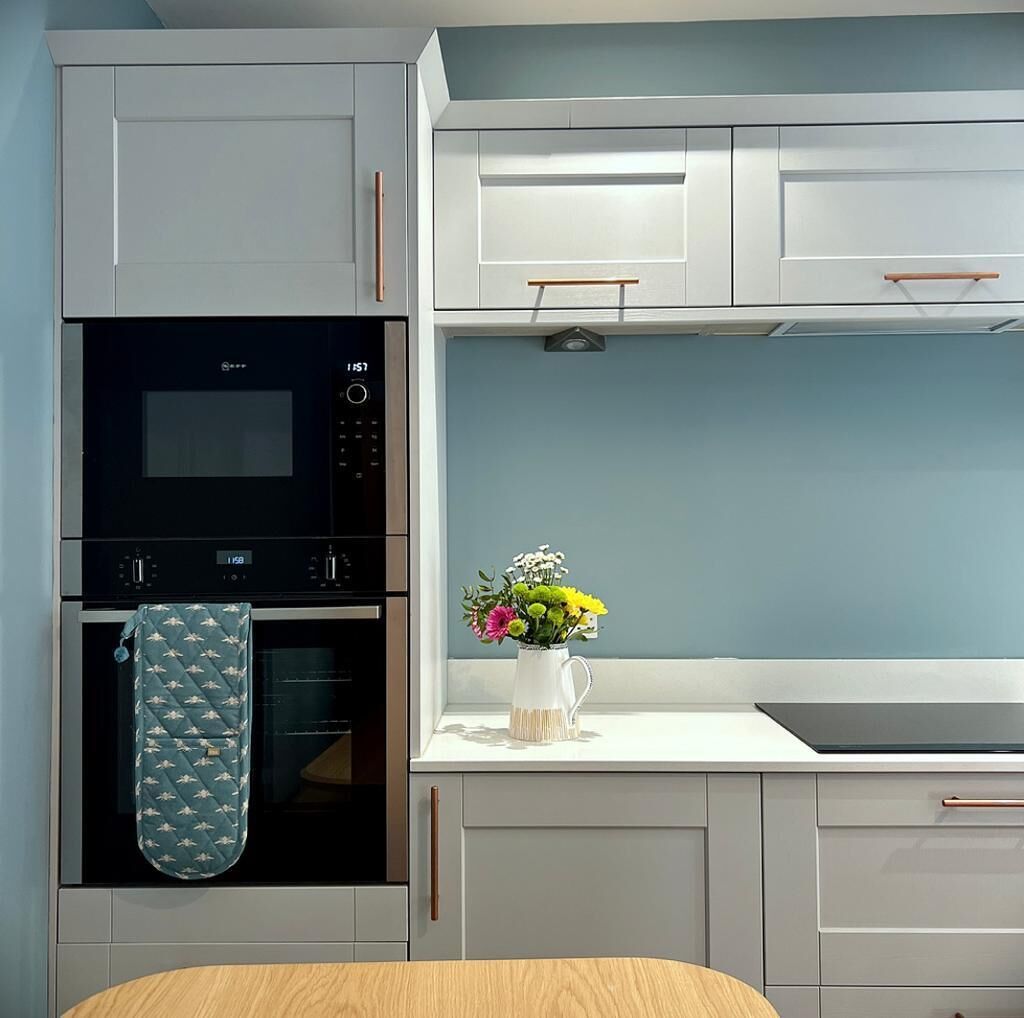 Eine moderne Küche mit weißen Schränken, einem schwarzen Backofen und einer Vase mit Blumen auf der Arbeitsfläche.