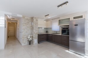 Una cocina moderna con refrigerador de acero inoxidable, muebles oscuros y una pared decorativa de piedra.