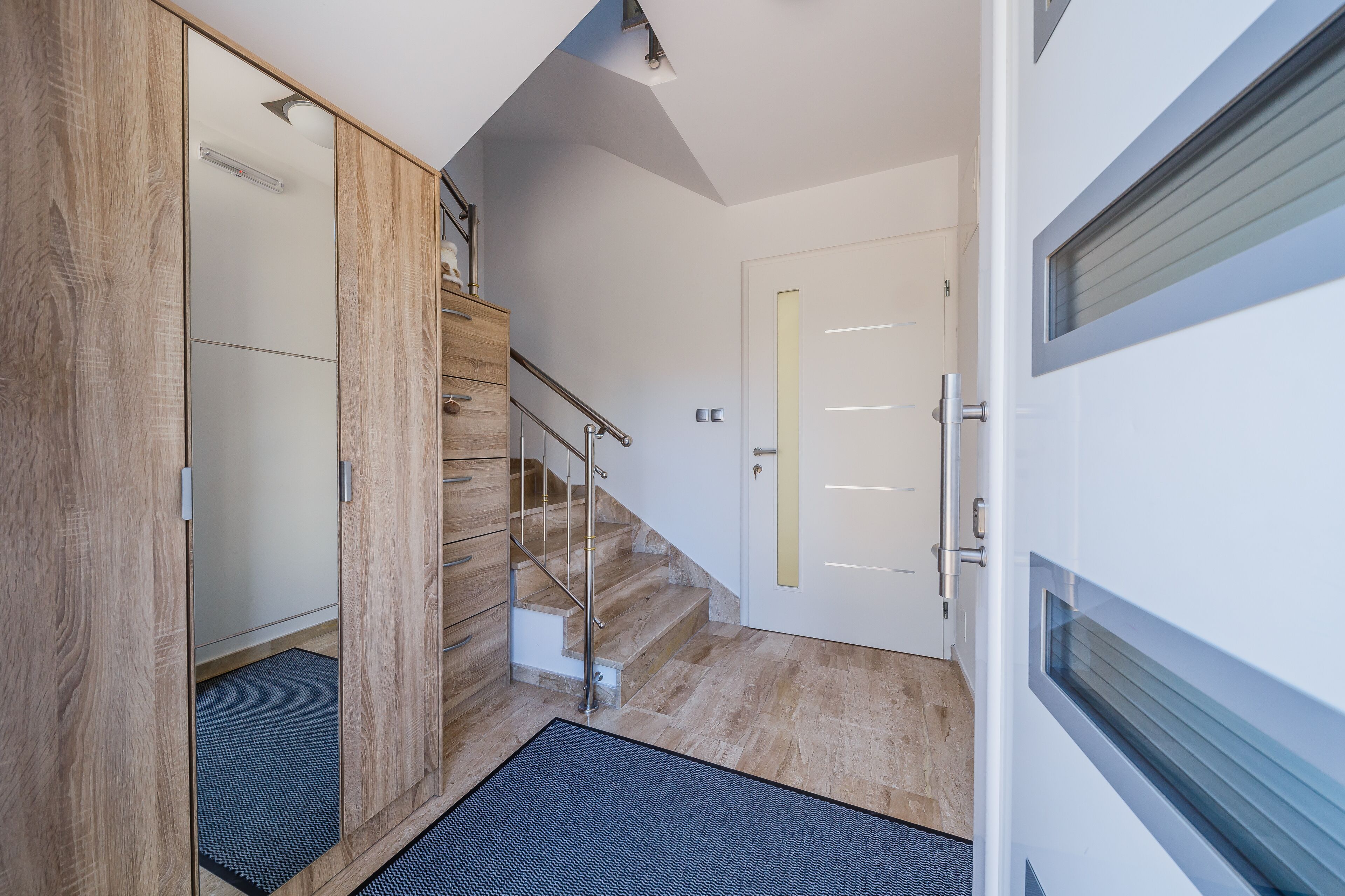 Ein modernes Interieur mit einem Holzschrank, einer Treppe und einer weißen Tür mit Fenster.