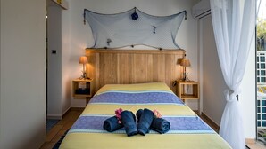 Una cama bien tendida con toallas enrolladas y flores, cabecera de madera, lámparas de noche y vistas al exterior.