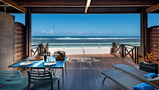 Una terraza con una mesa preparada para dos, con vista a una playa y una barandilla.