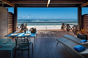 Une terrasse avec une table dressée pour deux personnes, donnant sur une plage et agrémentée d’une rambarde.