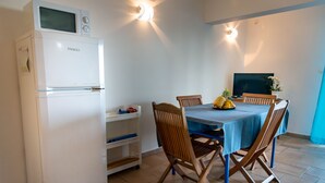 Cocina funcional con refrigerador blanco, mesa de comedor con mantel azul, sillas de madera y televisor sobre un mueble.