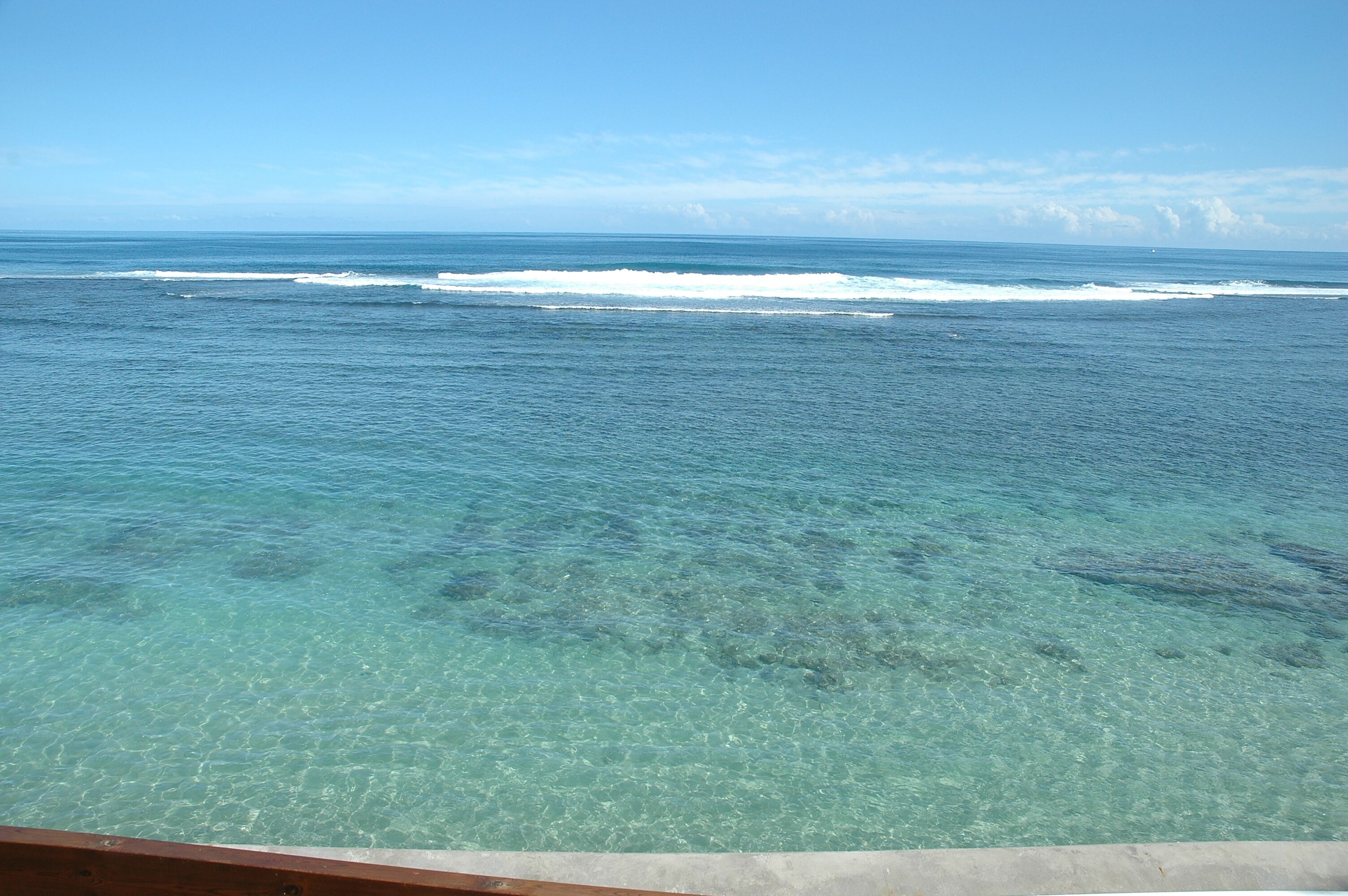 Une vue dégagée sur l’océan, avec ses vagues, une terrasse en bois et une bordure en béton.