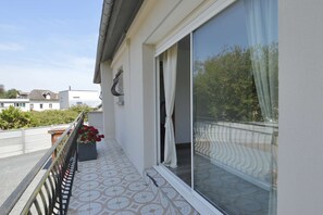 Un balcon doté d’un sol à motifs, un pot de fleurs avec des fleurs rouges, et une vue sur un quartier résidentiel.