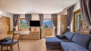Una sala de estar moderna con sofá, televisor, muebles de madera y ventanas grandes.