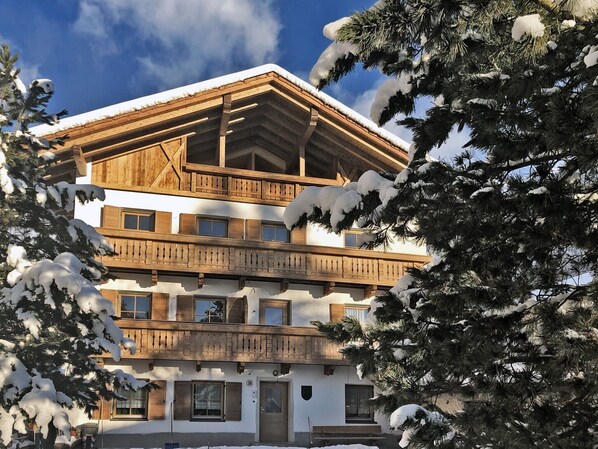 Un chalet à plusieurs étages, doté de balcons en bois et entouré d’arbres couverts de neige.