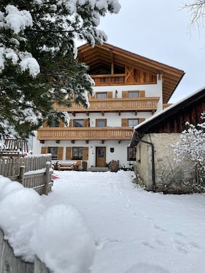 Un chalet de dos pisos con balcones de madera, techo cubierto de nieve y valla de madera en primer plano.